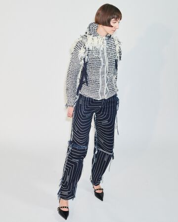 STEM design look: A person posing in a white and dark grey abstract zero-waste woven jacket paired with matching loose woven trousers
