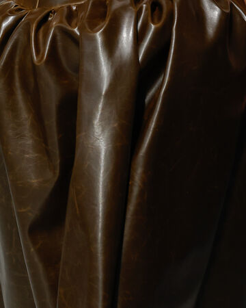 Material close-up of deeply gathered, rich dark brown plant-based alternative leather
