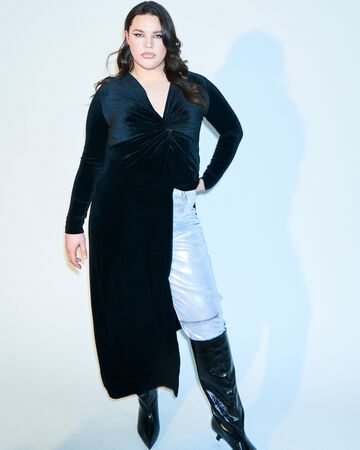 Alectra Rothschild design look: A person posing in a long black velvet asymmetrical tunic top styled over contrasting light blue denim trousers